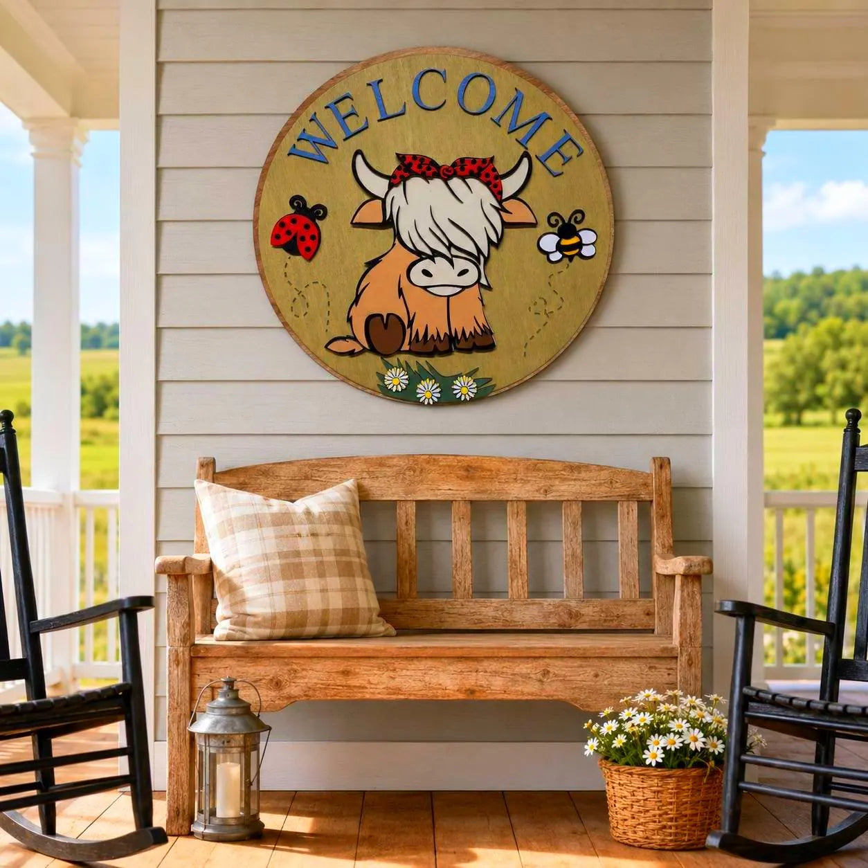 Highland cow Welcome wood sign displayed above a rustic bench between black rocking chairs on a sunny farmhouse porch.