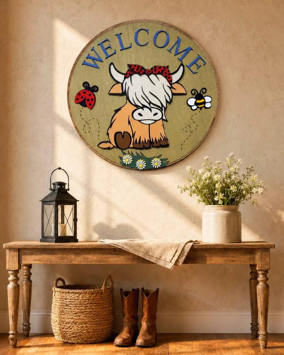 Layered Highland cow Welcome sign above an oak entry table styled with a lantern, wildflowers, woven basket and leather boots.
