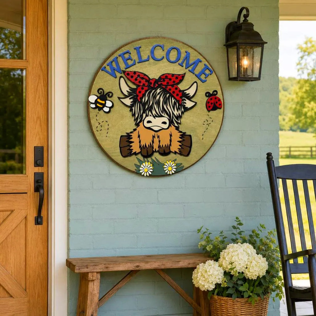 Shaggy Highland cow Welcome sign with a red polka-dot bow displayed on a pale blue brick farmhouse porch beside a Dutch door.
