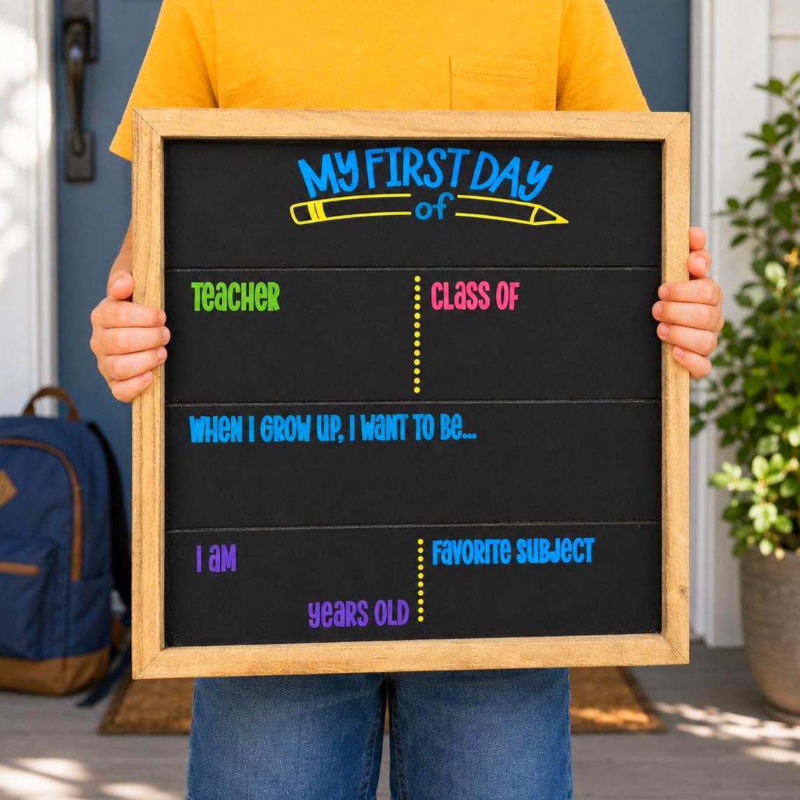 Child in a yellow shirt holding a blank 16x16 My First Day chalkboard sign with spaces for teacher, class year, age and favorite subject.