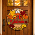 Close-up of a colorful layered wood turkey Welcome sign hanging on a stained wood front door with autumn trees reflected above.